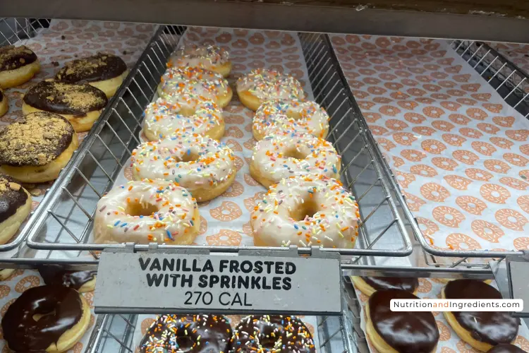 Display of Dunkin' vanilla frosted donuts with rainbow sprinkles.