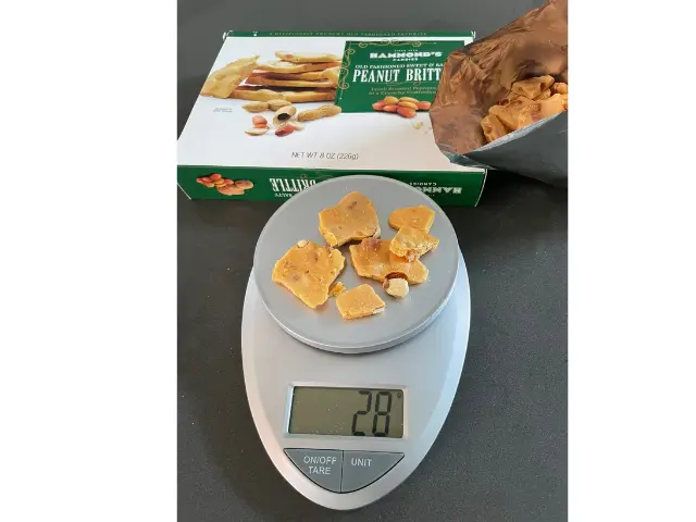 One serving size (28 grams) of peanut brittle on a food scale.