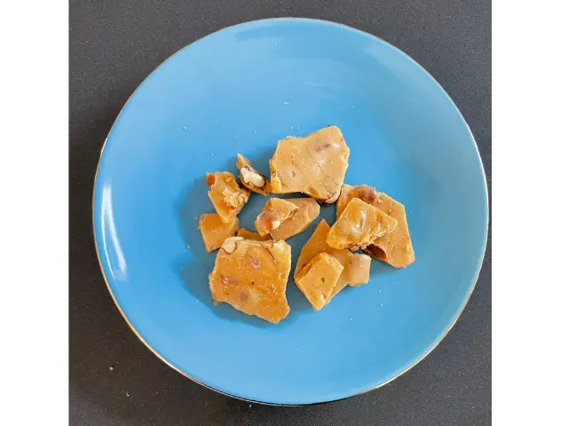 A few pieces of peanut brittle served on small blue plate.