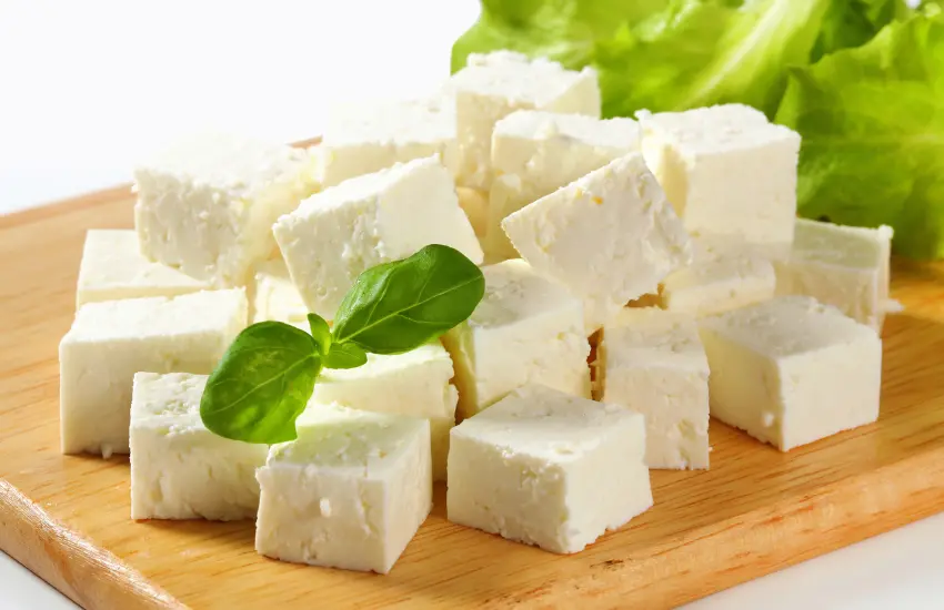 Cubed feta cheese on wood cutting board.