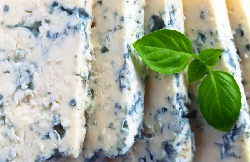 Sliced firm gorgonzola and basil leaf.